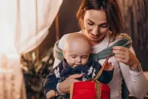 Mamãe de primeira viagem com seu bebê no colo abrindo um presente